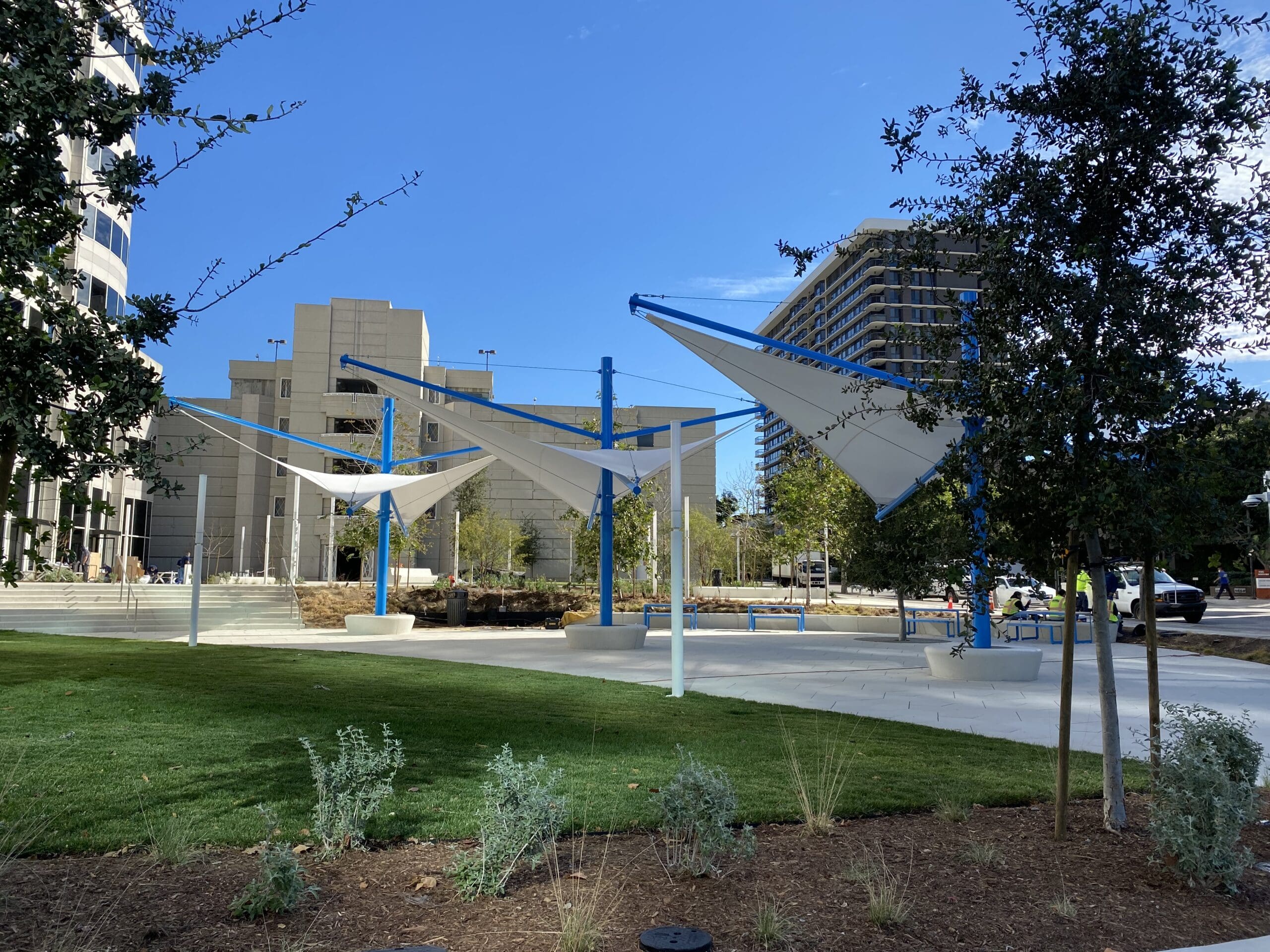 Modern outdoor USA Shade Aurora Shade with blue and white structure in a park setting with buildings in the background.