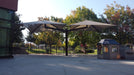 USA Shade Single Post Cantilever Shade Structure custom double umbrella at a park with trees and a building in the background.