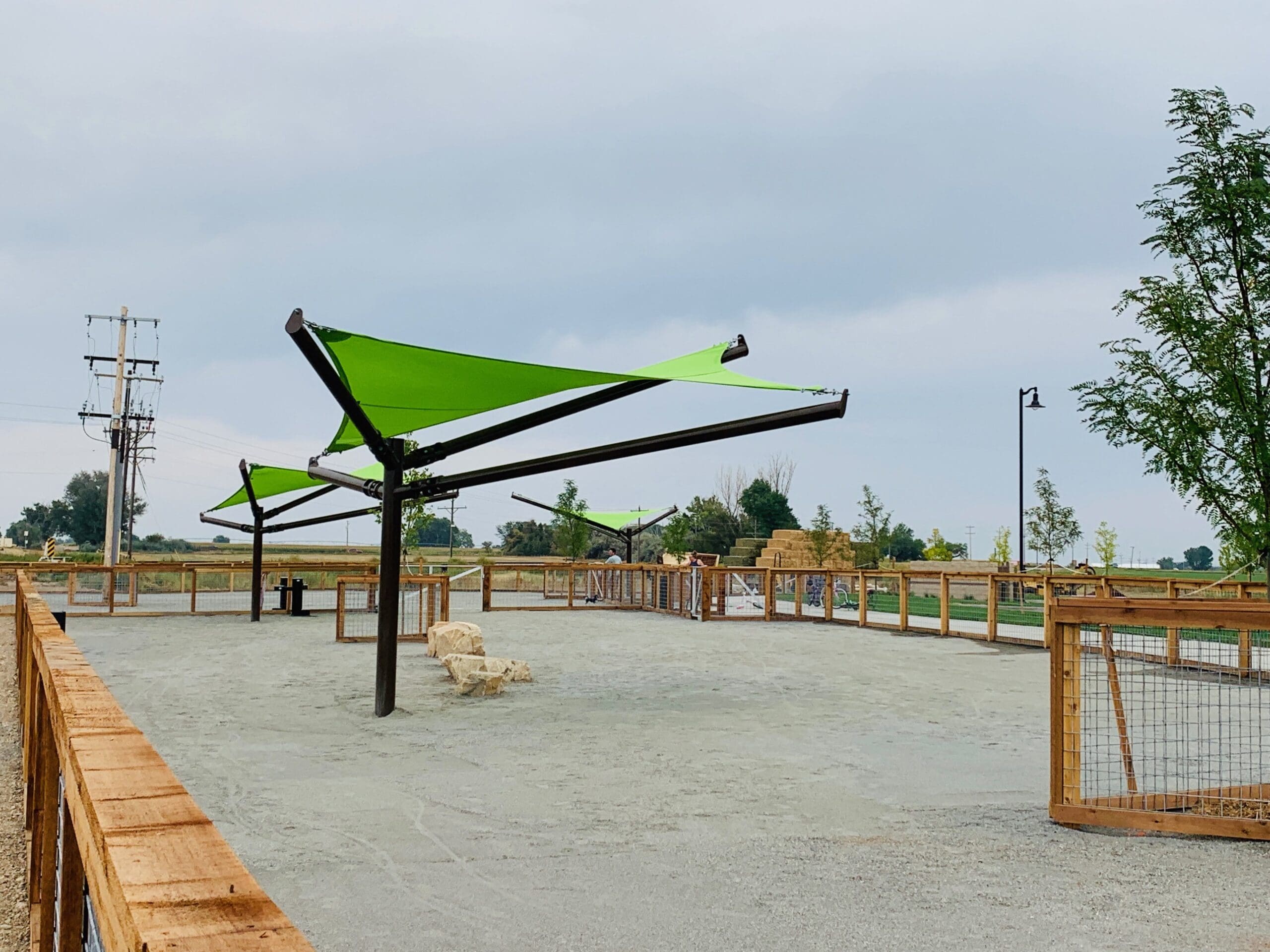 Outdoor area with green USA Shade Arbor Shade sails and wooden benches under a clear sky.