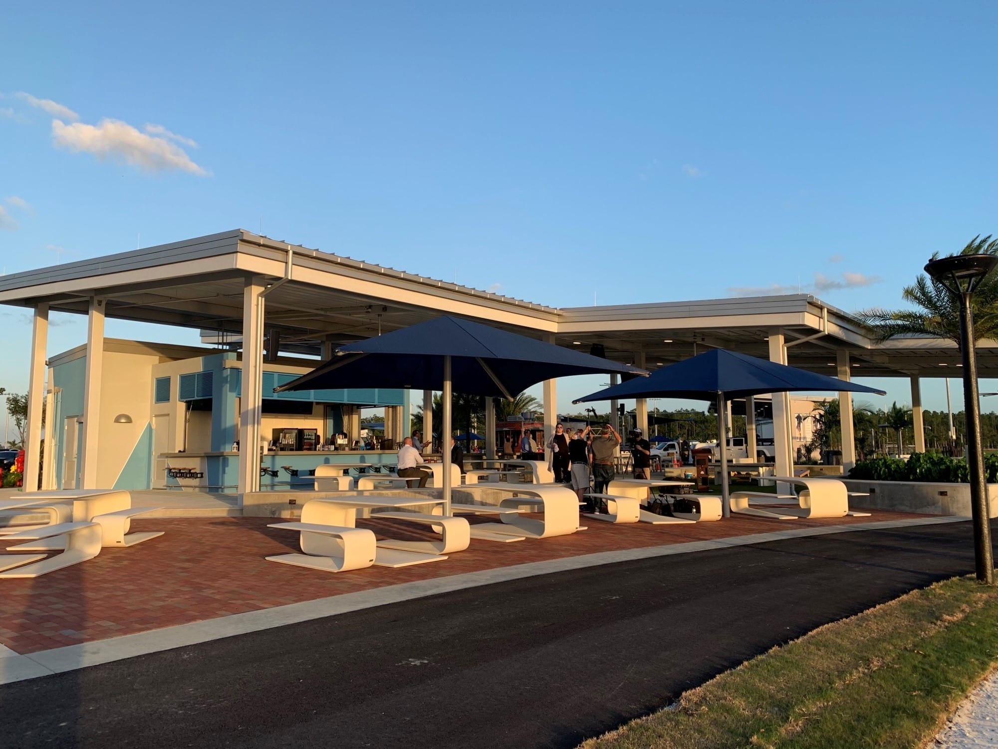 Outdoor seating area with tables and Blue USA Shade Single Post Pyramids at a park or recreational facility.