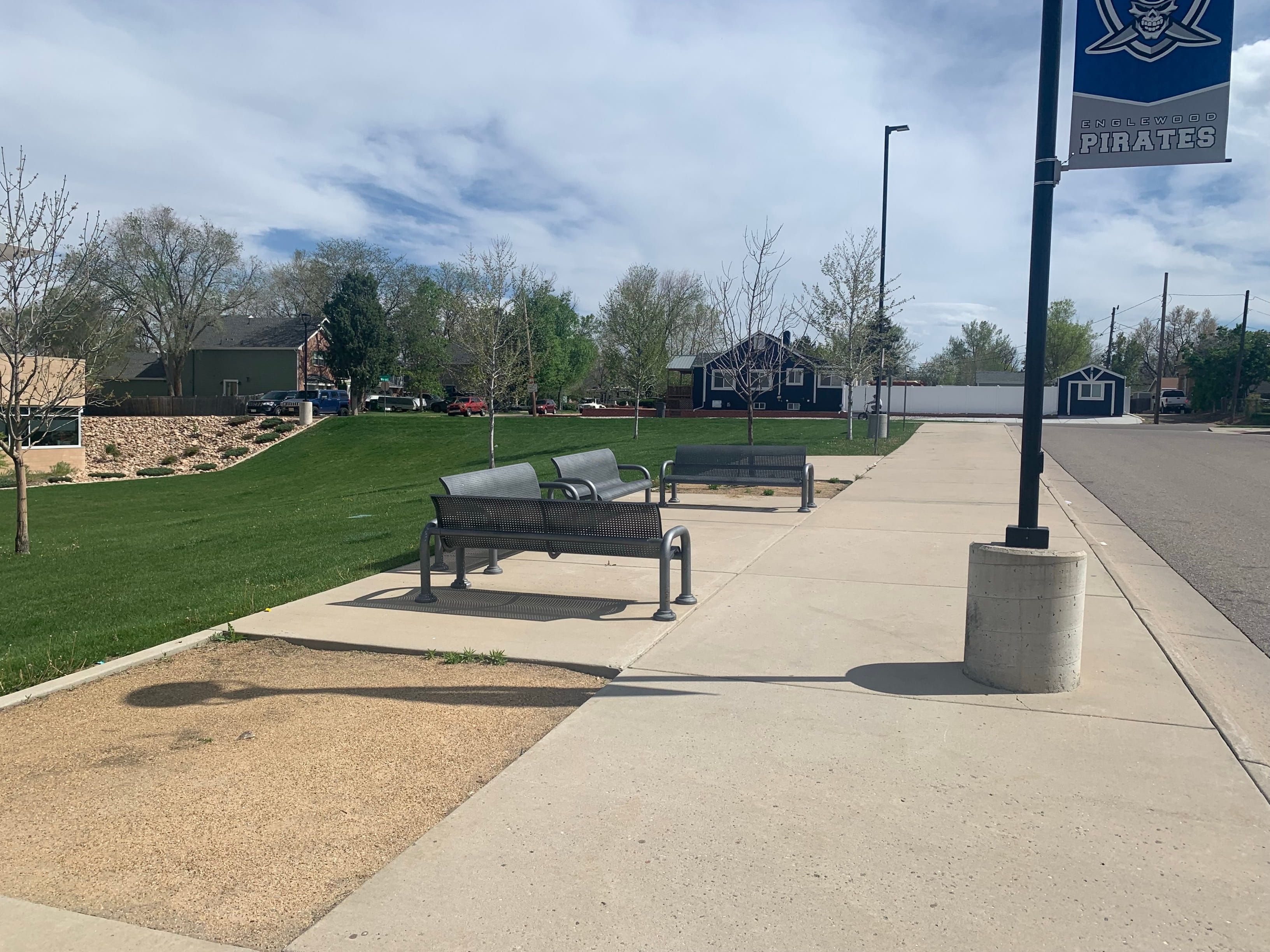 Black and Silver Wabash Valley Contemporary Perforated Steel Bench Surface Mount along a school park sidewalk, commercial park bench with back and arms