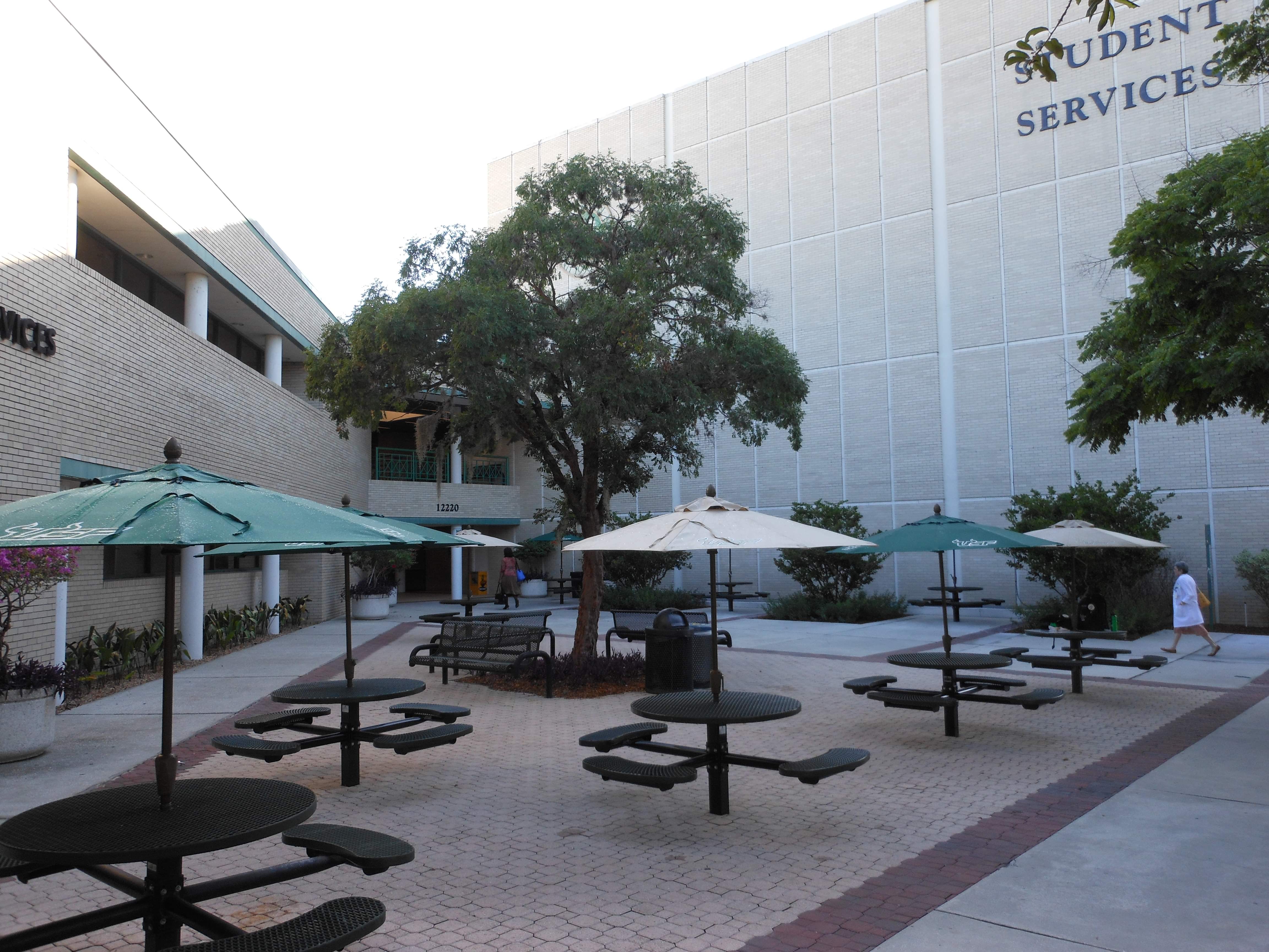 Black Wabash Valley Signature Round Pedestal Picnic Tables with Diamond tops set inground in a university courtyard with patio umbrellas, contract outdoor furniture