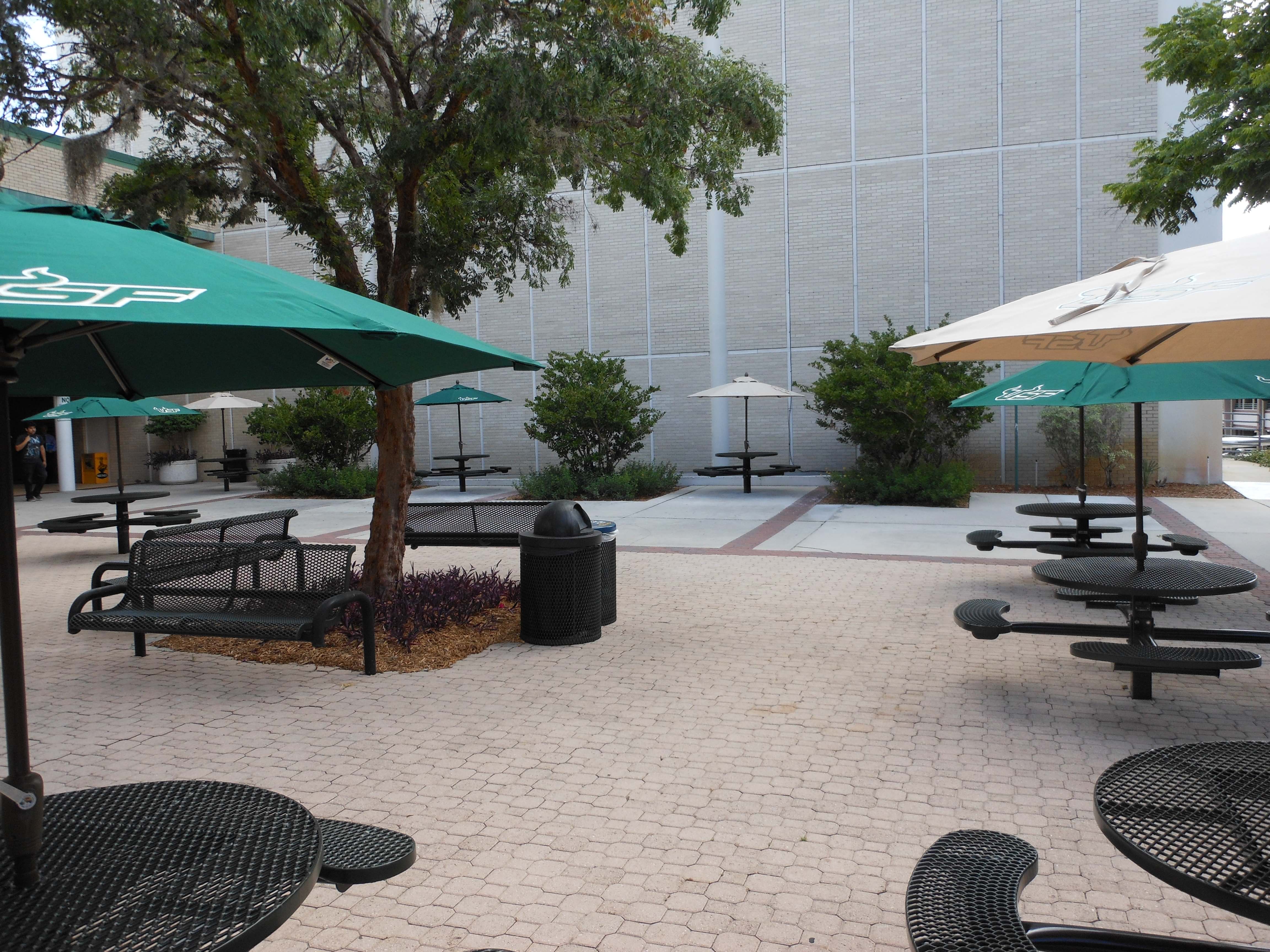 Black Wabash Valley Signature Round Pedestal Picnic Tables with Diamond tops and patio umbrellas in a campus courtyard, round outdoor metal table