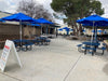 Blue Wabash Valley Signature Square Picnic Tables under blue umbrellas in a school lunch court, picnic tables with separate benches