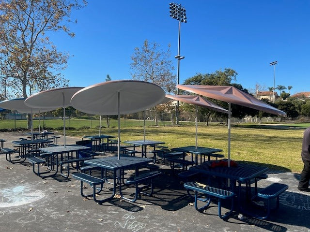 Blue Wabash Valley Signature Square Picnic Tables with Diamond tops and umbrellas beside a school sports field, a square metal picnic table
