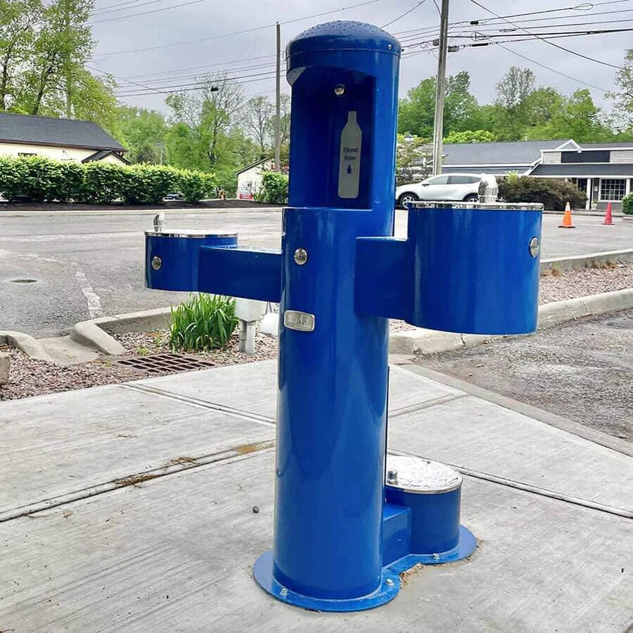 Blue Willoughby Tri-level Drinking Fountain with Bottle Filler and Pet Drinking Fountain on a sidewalk with a road and buildings in the background.