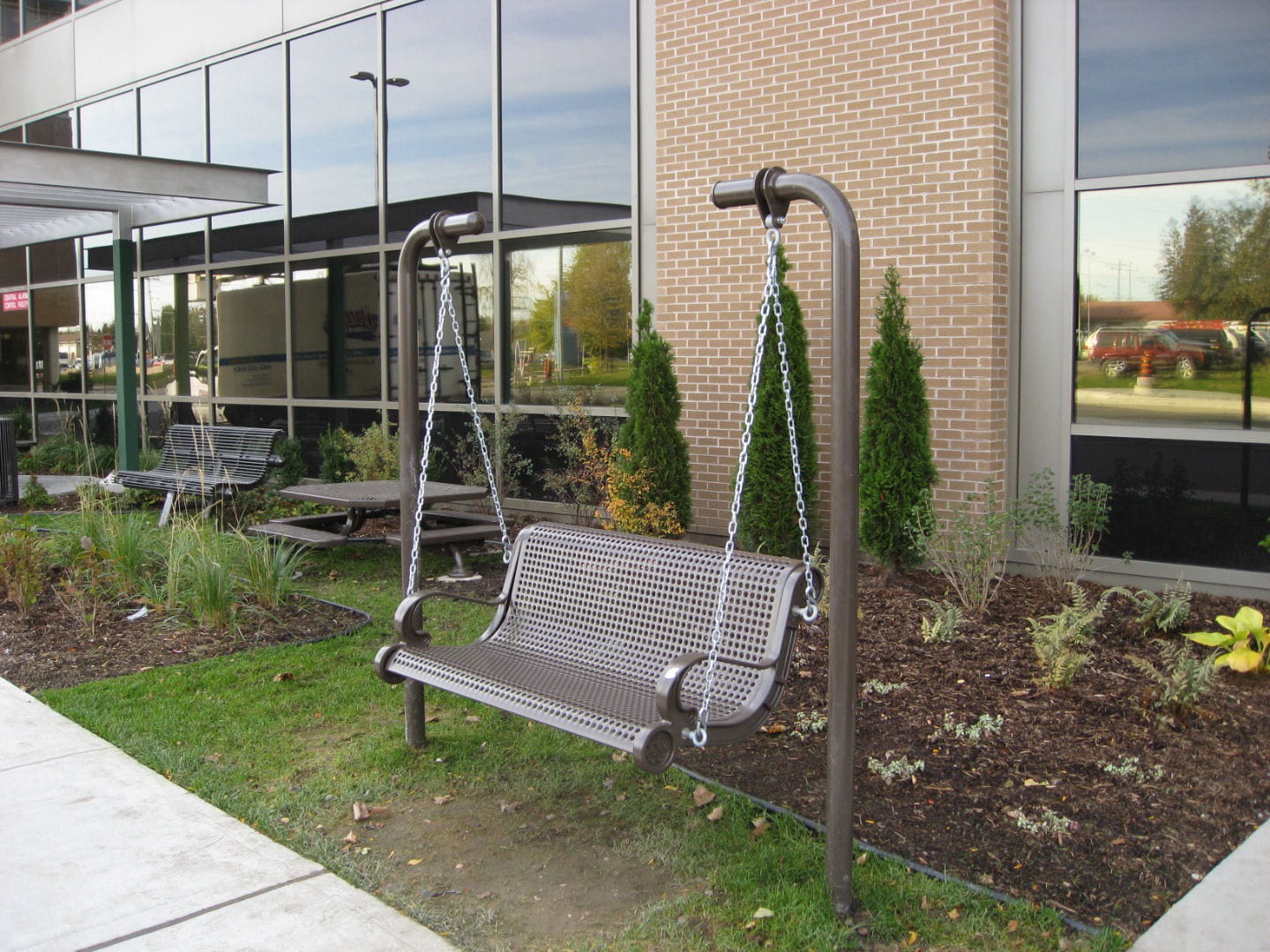 Brown Wabash Valley Estate Perforated Swing Bench, plastisol-coated steel seat installed inground at a hospital healing garden, commercial swing