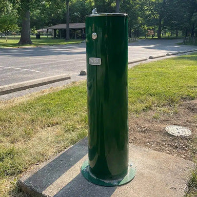 Green Willhoughby Single Outdoor Drinking Fountain on a concrete slab in a park setting Lifestyle Image
