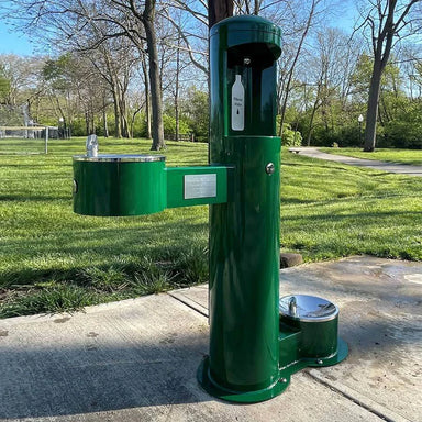Green Willoughby Stainless Side Approach Bottle Filler Drinking Fountain in a park setting with grass and trees.