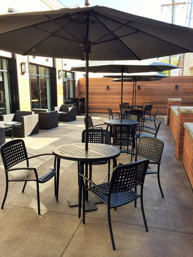 Black Hanna perforated dining chairs with arms around round slat tables under umbrellas on a courtyard patio, model HA911AP, restaurant chairs