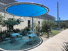 Outdoor seating area with blue USA Shade Cantilever Disc shade structures and tables under a clear blue sky.