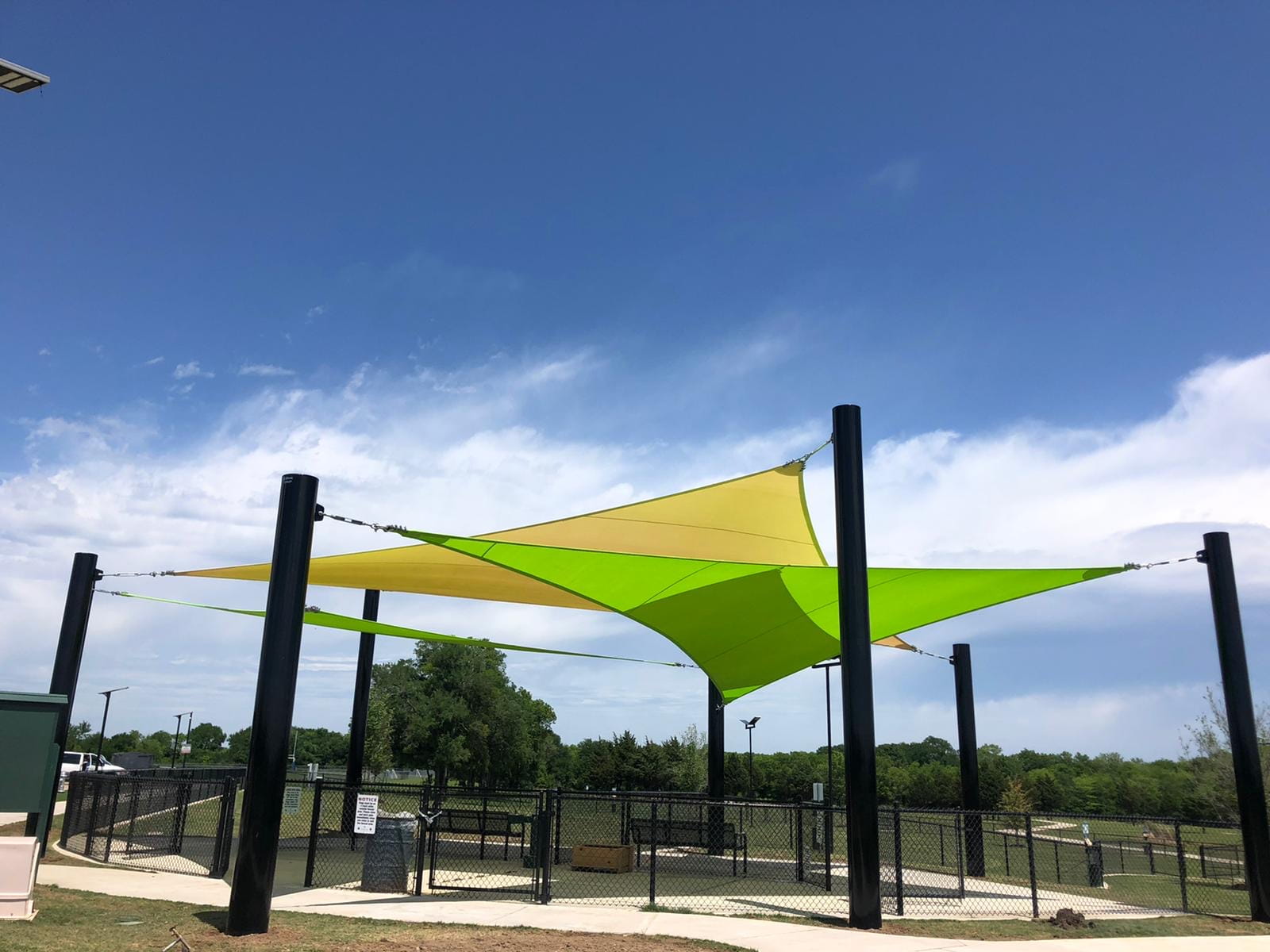 Green and yellow 3-point shade sail structure against a blue sky with white clouds.