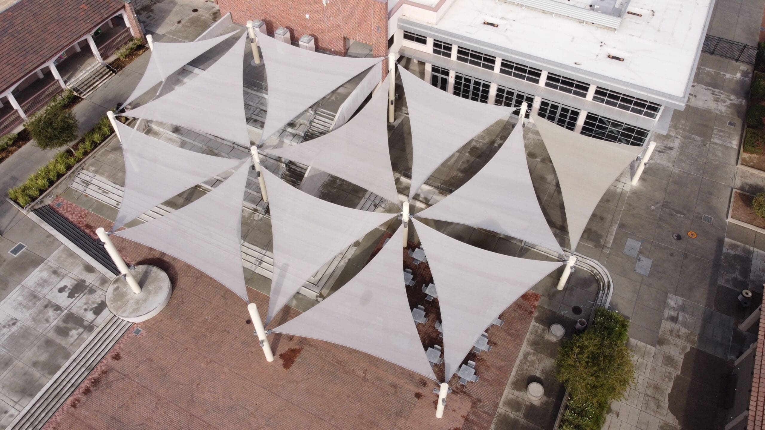 Aerial view of large white geometric 3- point shade sails in a courtyard.