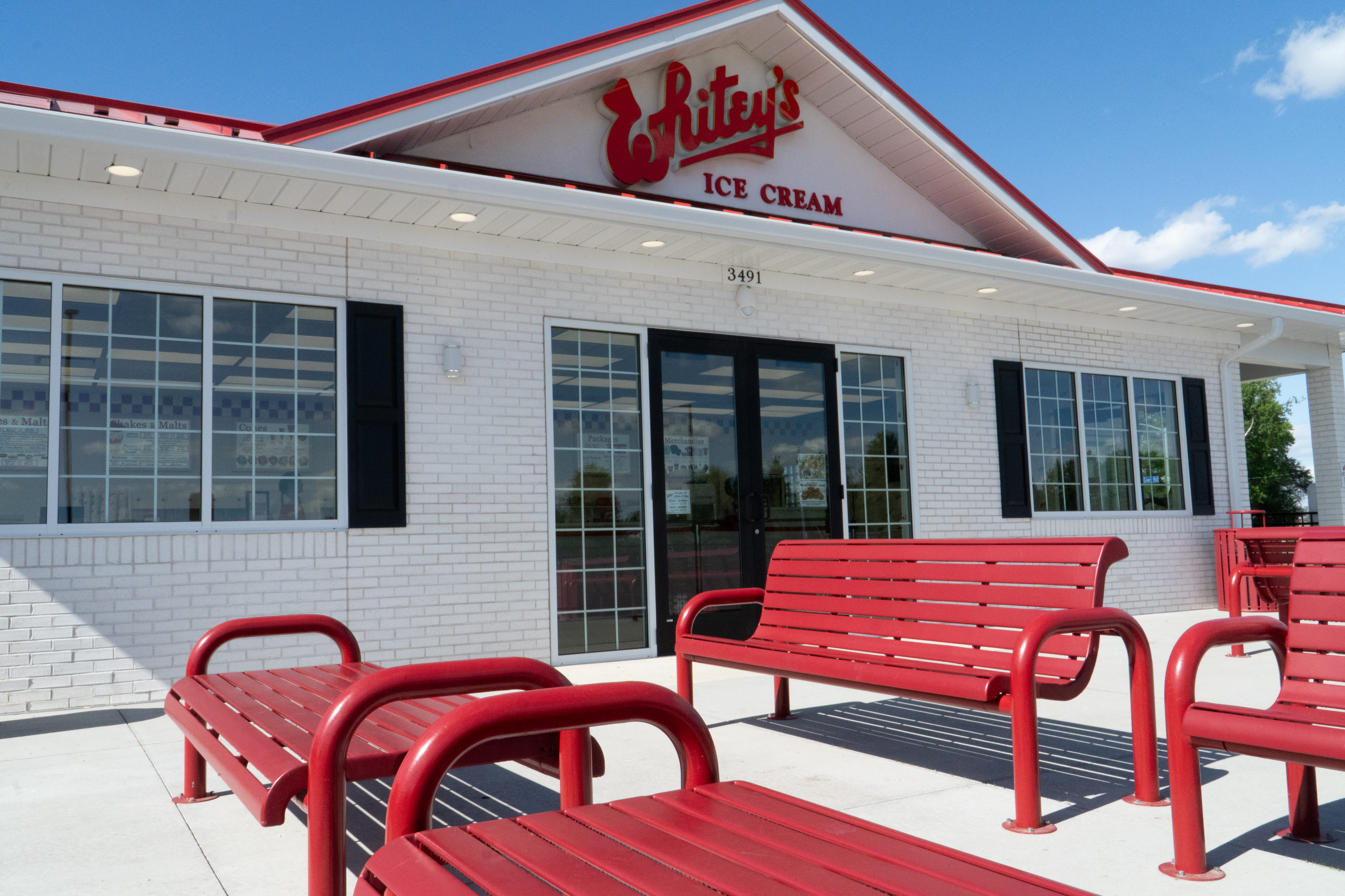Red Wabash Valley Contemporary Slatted Steel Benches Surface Mount outside an ice cream shop storefront, commercial grade outdoor bench seating