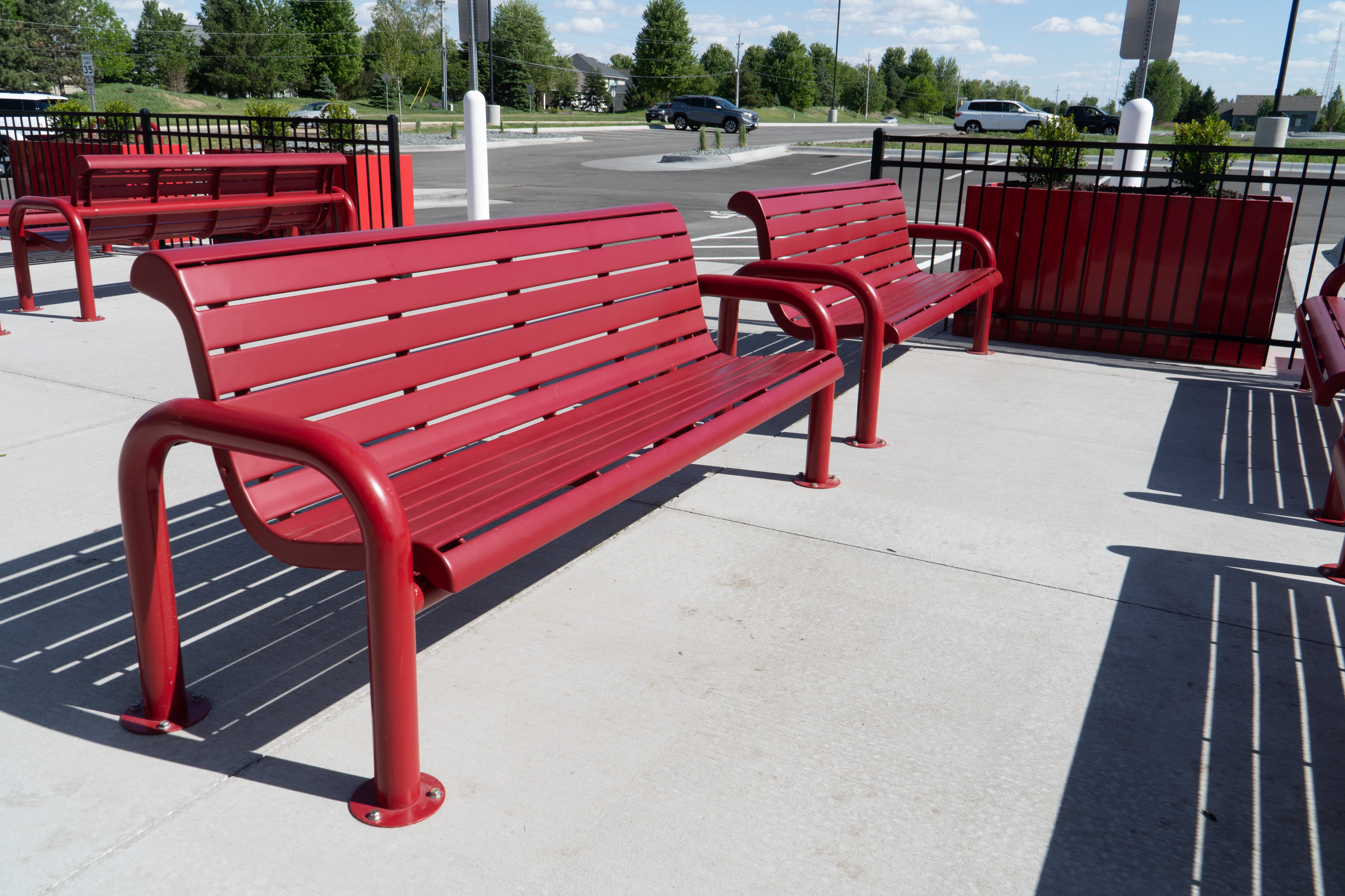 Red Wabash Valley Contemporary Slatted Steel Bench Surface Mount anchored to a concrete patio, heavy duty park bench seating with arms