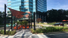 Outdoor seating area with red shade sails in front of a modern building