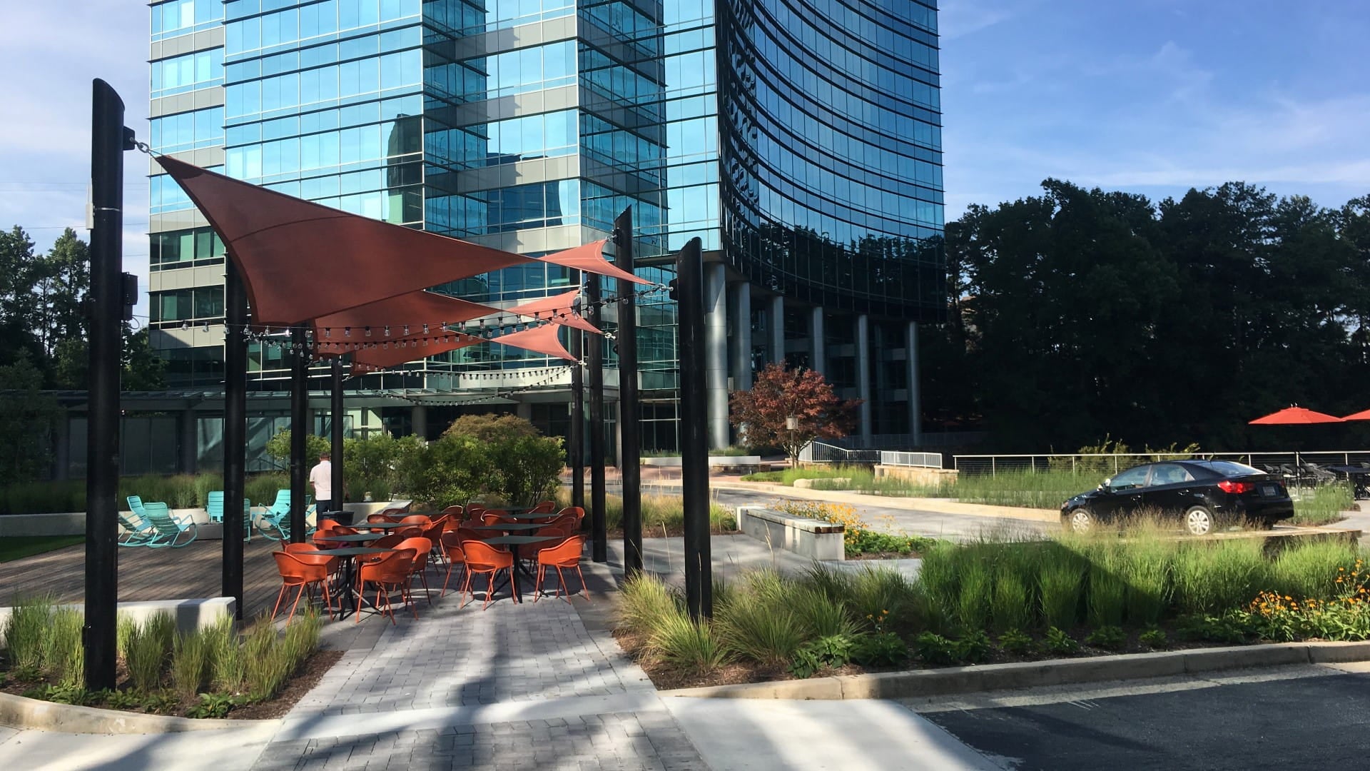 Outdoor seating area with red shade sails in front of a modern building