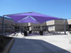 Outdoor seating area with a large purple USA Shade Super Span Multi-Panel Hip Shade on a sunny day.
