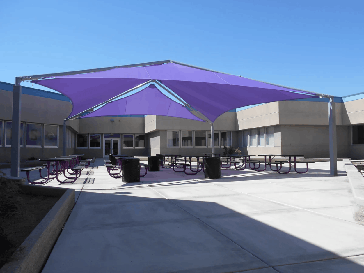 Outdoor seating area with a large purple USA Shade Super Span Multi-Panel Hip Shade on a sunny day.