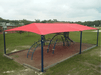 Playground with red USA Shade 6-Post Hip and playground equipment on a grassy area