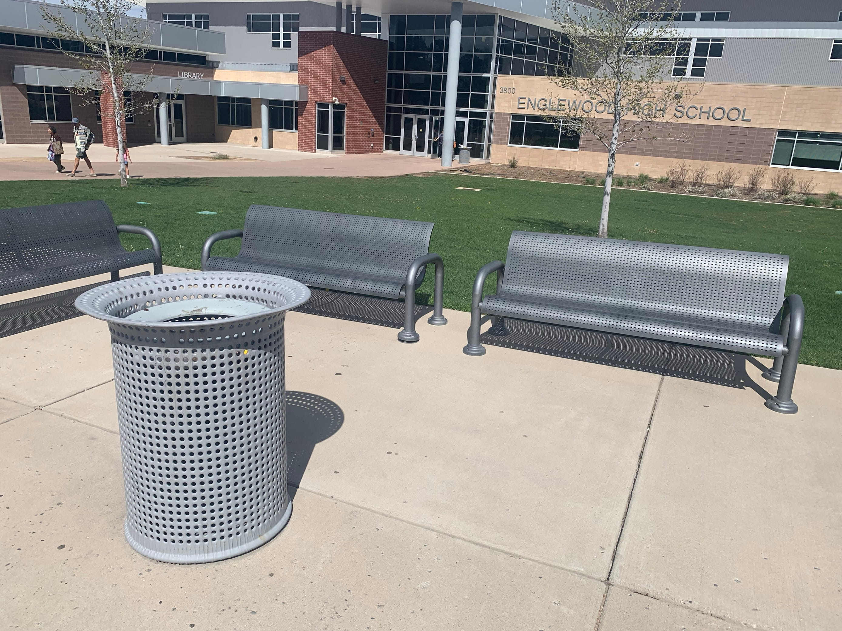 Silver Wabash Valley Contemporary Perforated Steel Benches Surface Mount with matching perforated trash receptacle on a high school campus plaza