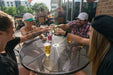 Friends toasting with beers around a black Sullivan round steel mesh patio table on a bar patio, outdoor patio table