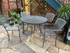 Silver Sullivan round steel mesh patio table with four stacking chairs on a flagstone courtyard, large round patio table