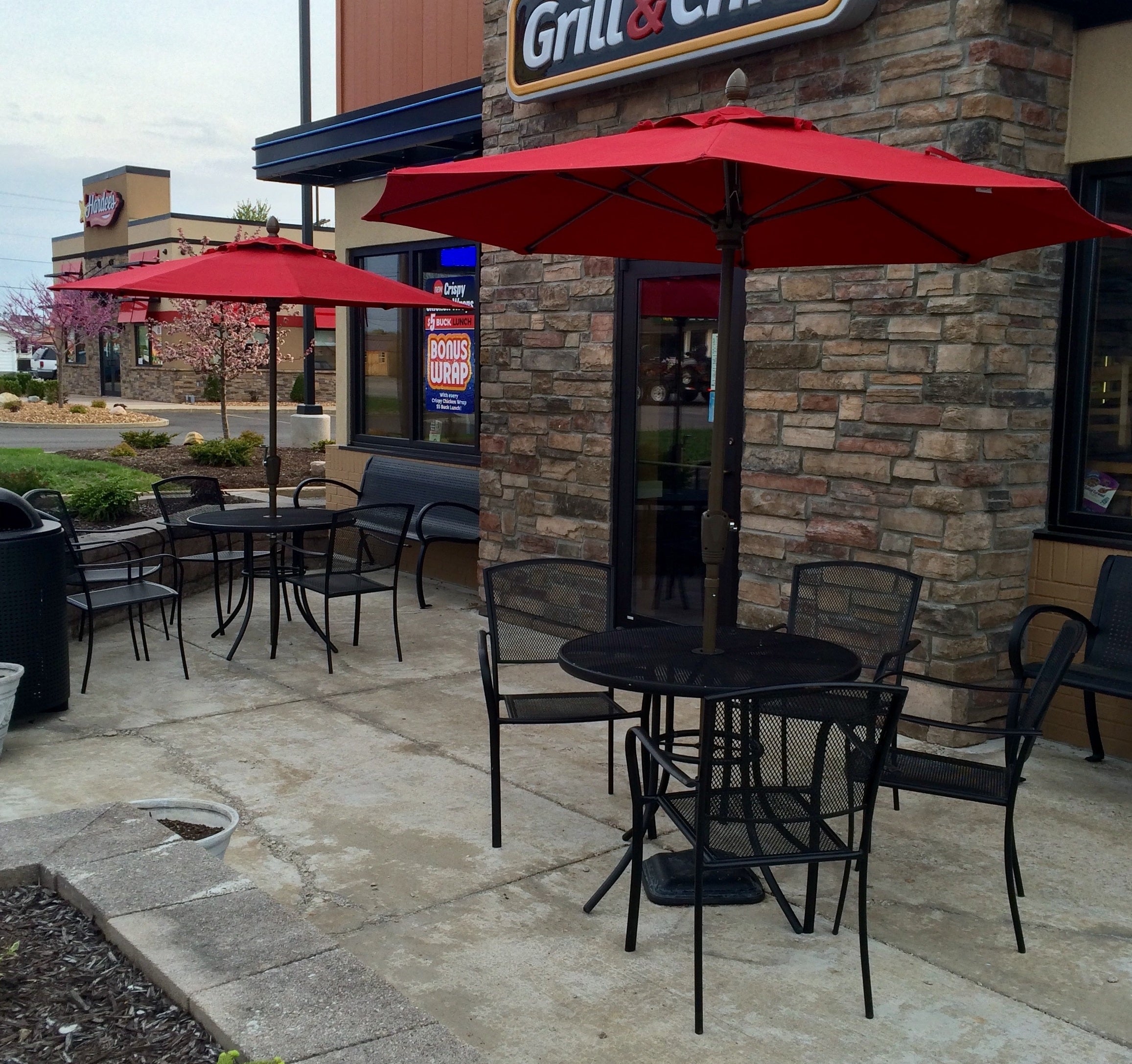 Black Sullivan round steel mesh patio tables and stacking chairs under red umbrellas outside a restaurant, outdoor patio table