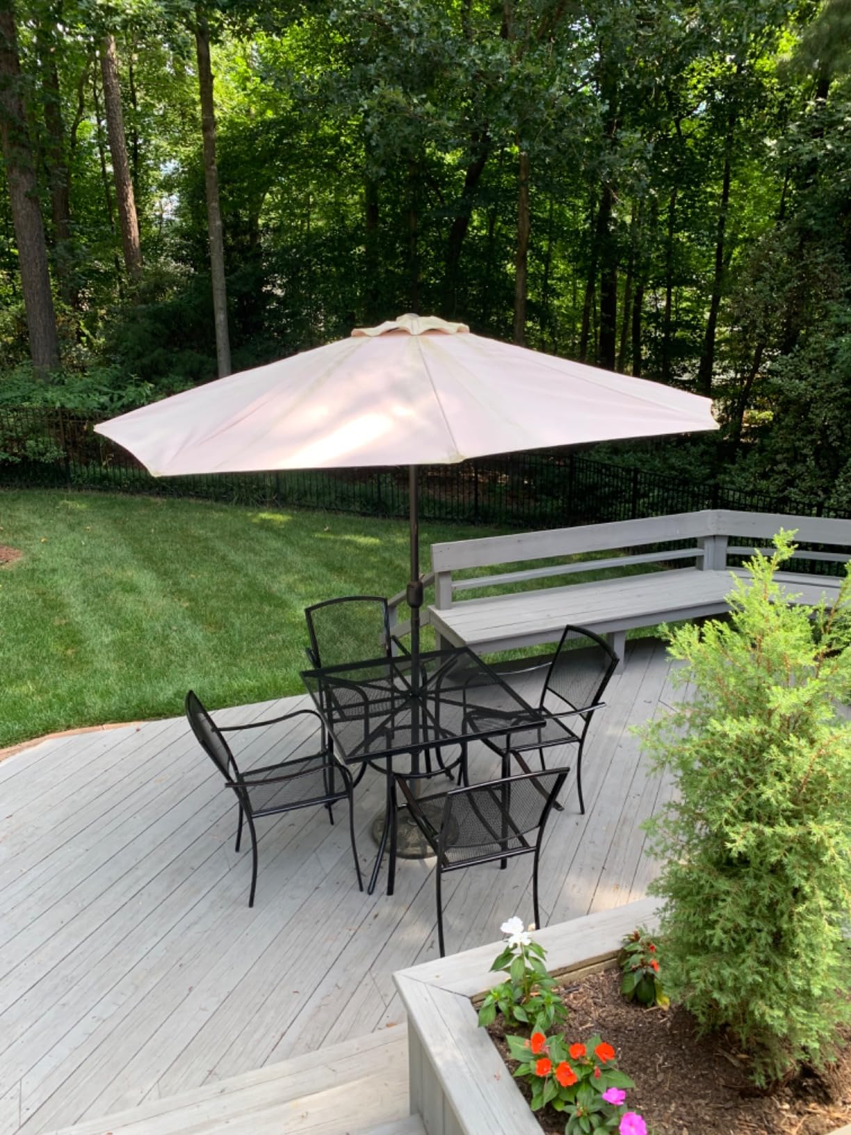 Black Sullivan square steel mesh patio table with four stacking chairs and an umbrella on a backyard deck, patio set for 4