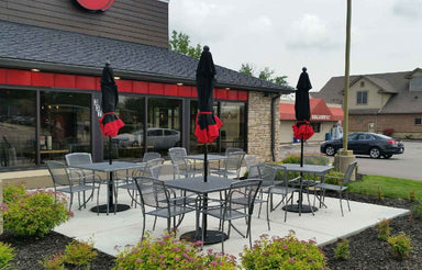 Silver Sullivan square steel mesh patio tables and stacking chairs with umbrellas on a restaurant patio, steel patio table