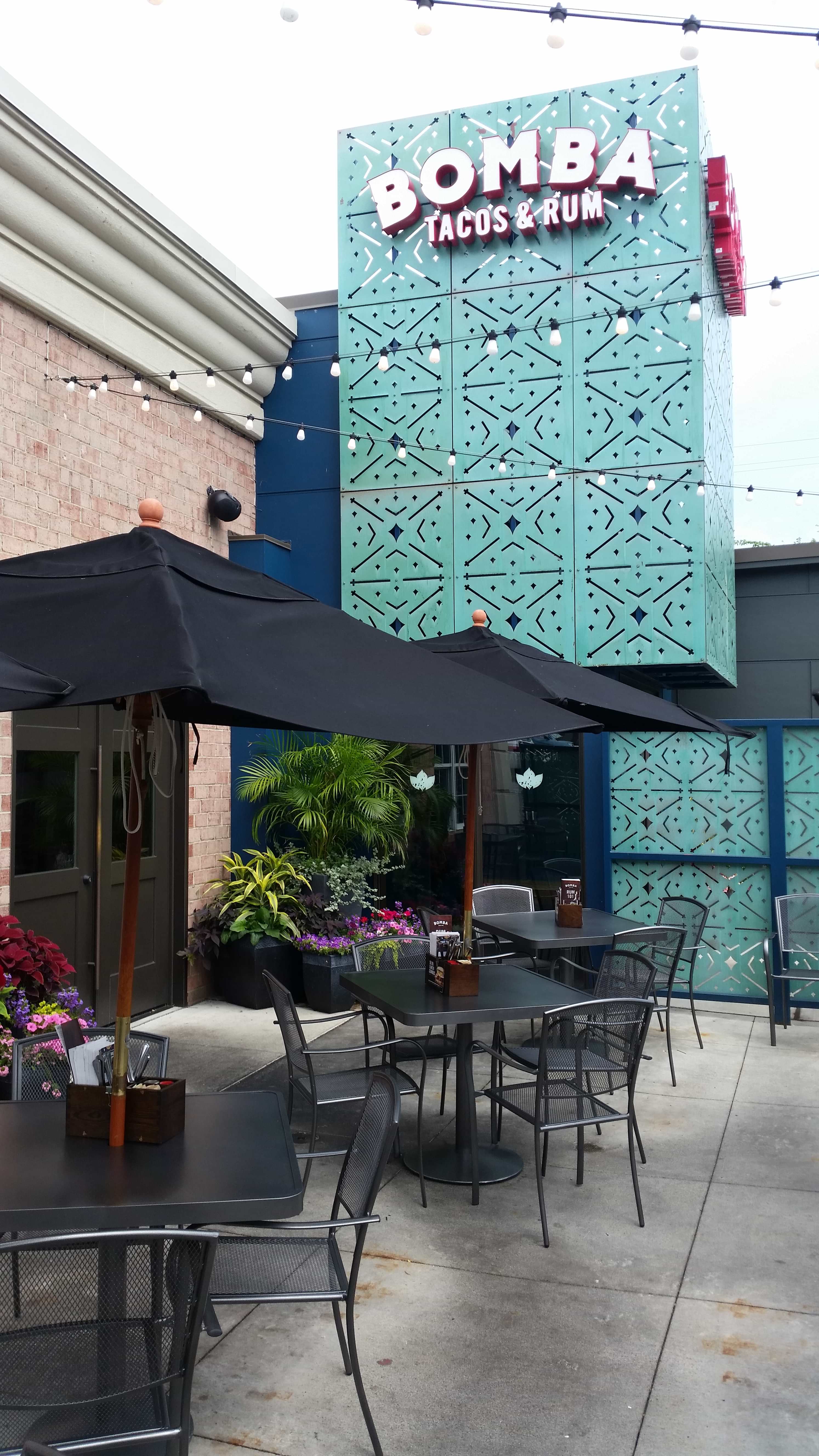 Black Sullivan stacking patio chairs at umbrella tables on a restaurant patio, steel patio chairs