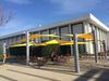 Outdoor seating area with yellow Sail Shades and tables in front of a building