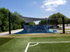 Outdoor sports facility with blue and white equipment under a shade sail, surrounded by trees and a clear sky.