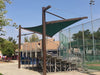 Outdoor setting with a green Cantilever Hypar Sail shade sail over a stage area, surrounded by trees and a fence.