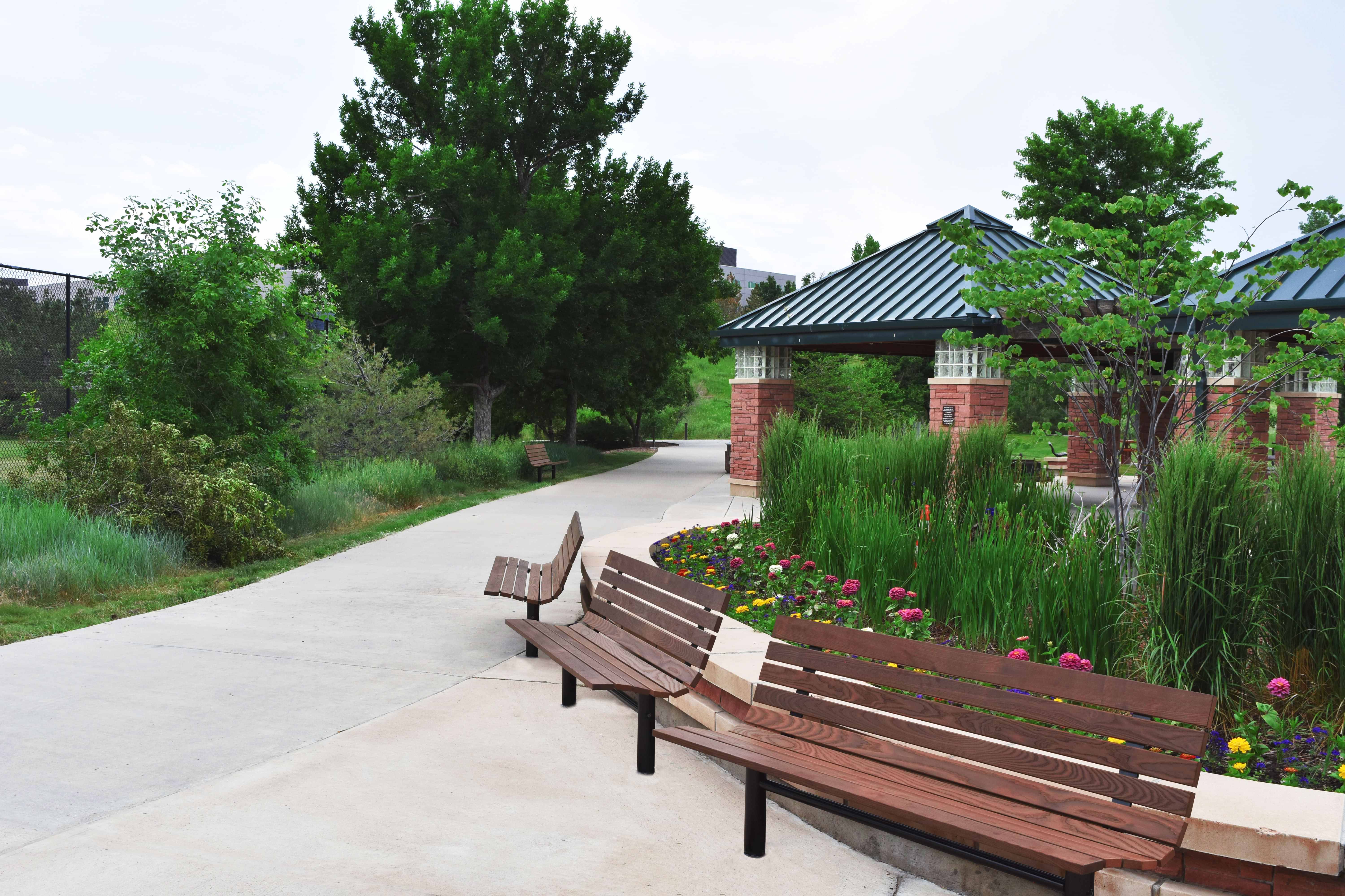 Wabash Valley Fairmount Wood Benches with Thermory ash slats on Inground posts along a park path and flower bed, model FA440N, commercial wood bench