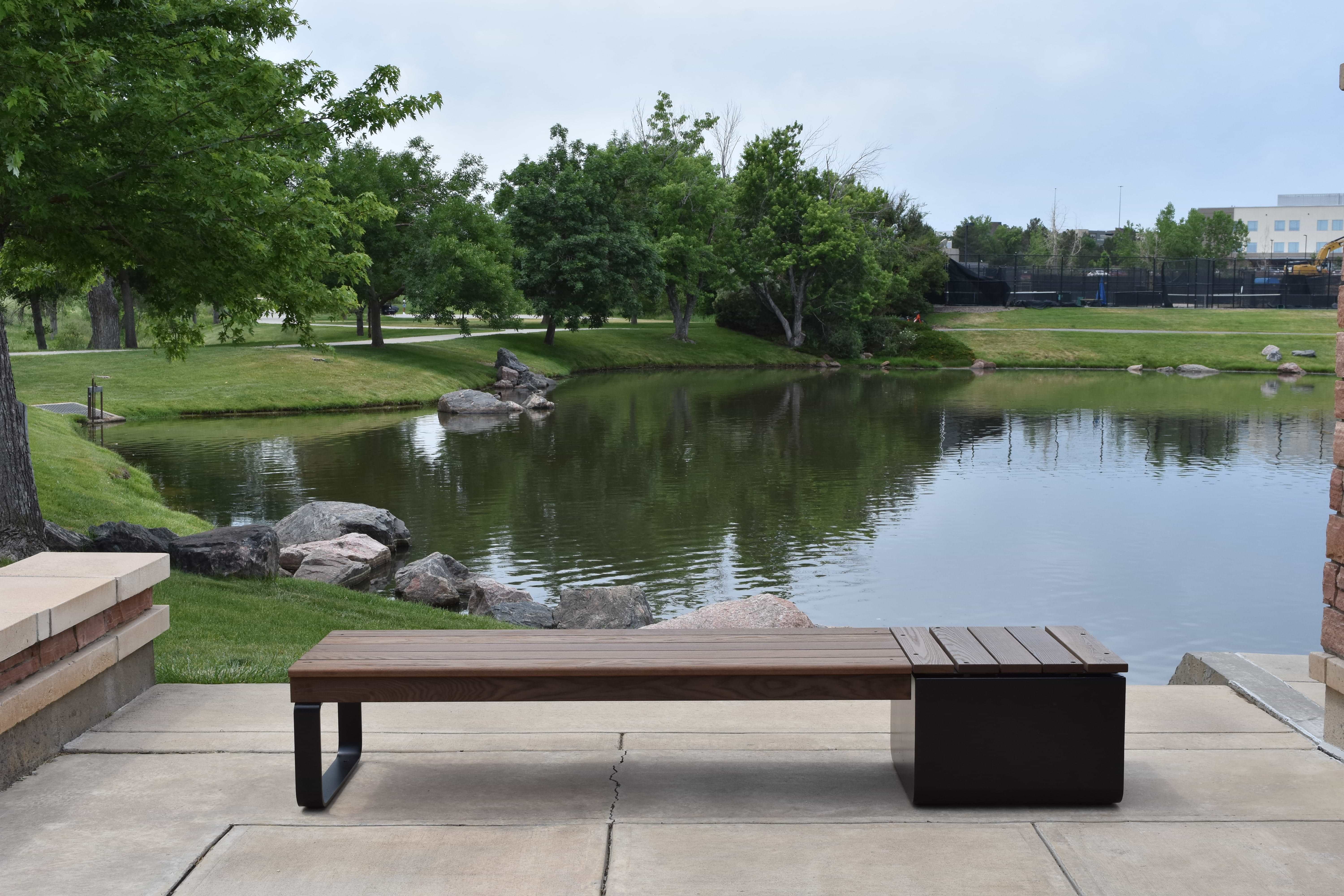 Wabash Valley Liberty Modular Bench with Square Seat facing a park pond, Thermory ash slats on black steel, model LBB002N, outdoor cube seating