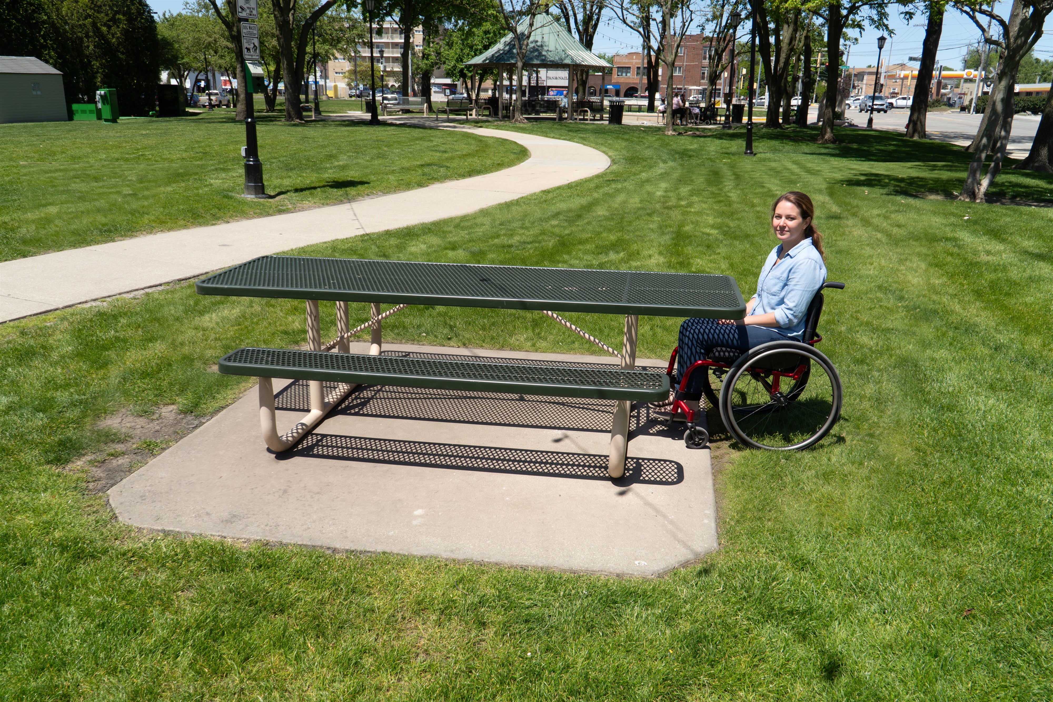 Guest in a wheelchair at the open end of a Wabash Valley Signature Portable Picnic Table, 8' ADA Accessible, green Diamond top on a tan frame, handicap picnic table