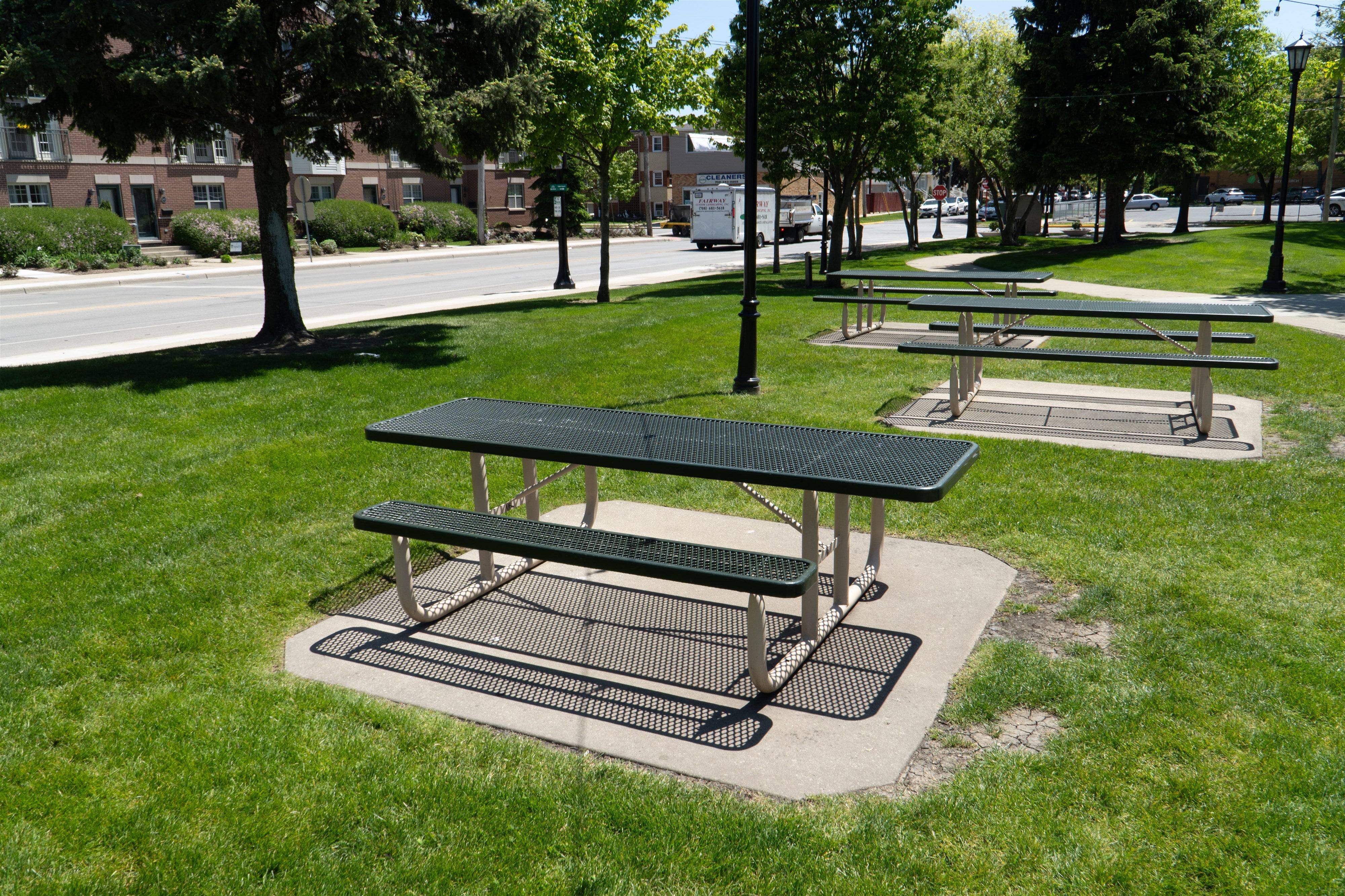 Wabash Valley Signature Portable Picnic Tables with green Diamond tops on tan frames, set on concrete pads in a town park, coated metal picnic table