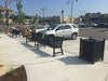 Black Wabash Valley Yorktown Aluminum Benches along a shopping plaza sidewalk beside a matching black trash receptacle, model YO1113C, metal patio bench