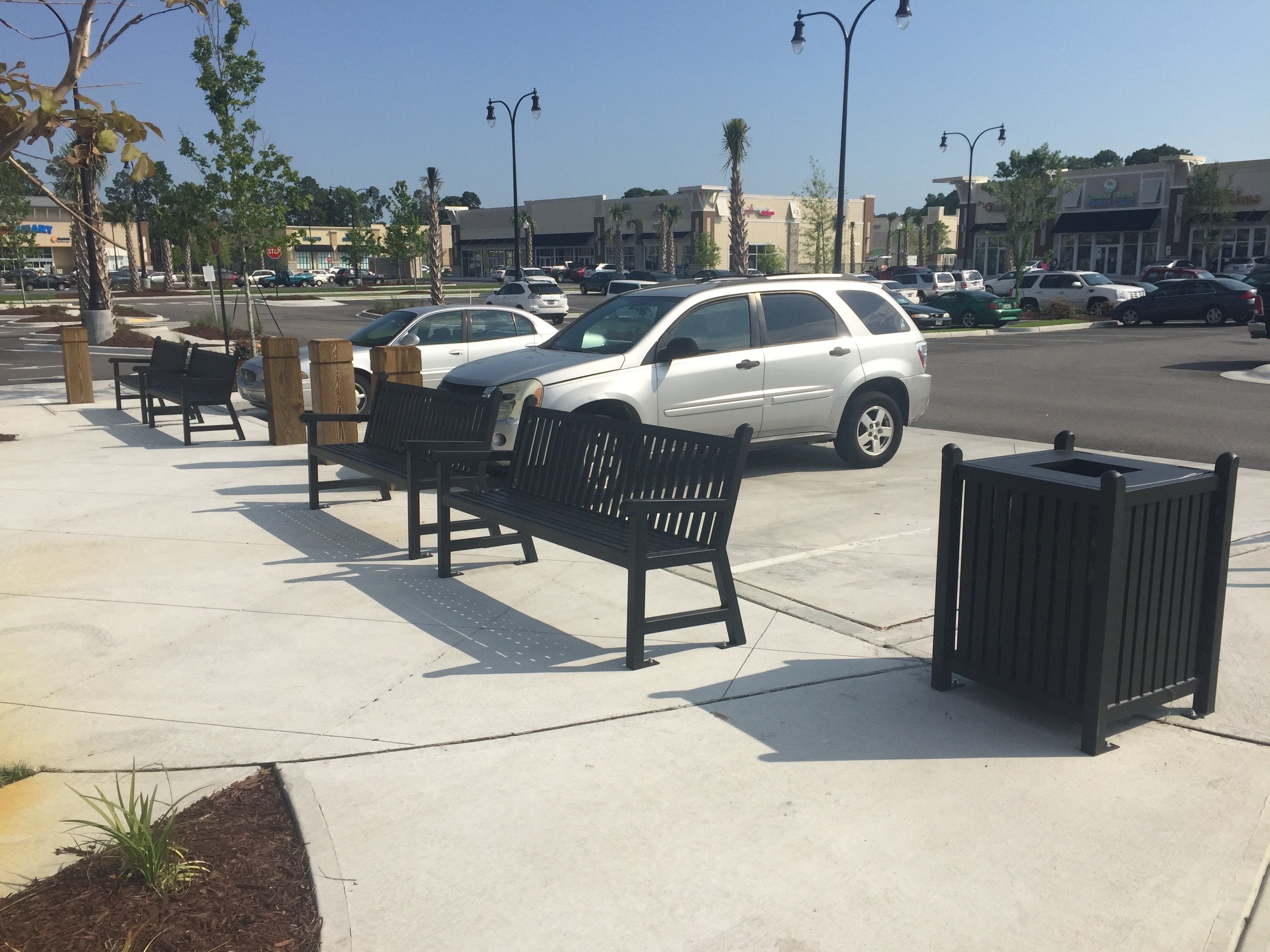 Black Wabash Valley 32 Gal. Yorktown Trash Receptacle beside matching Yorktown benches on a shopping plaza sidewalk, model YO3F33C, decorative outdoor trash can