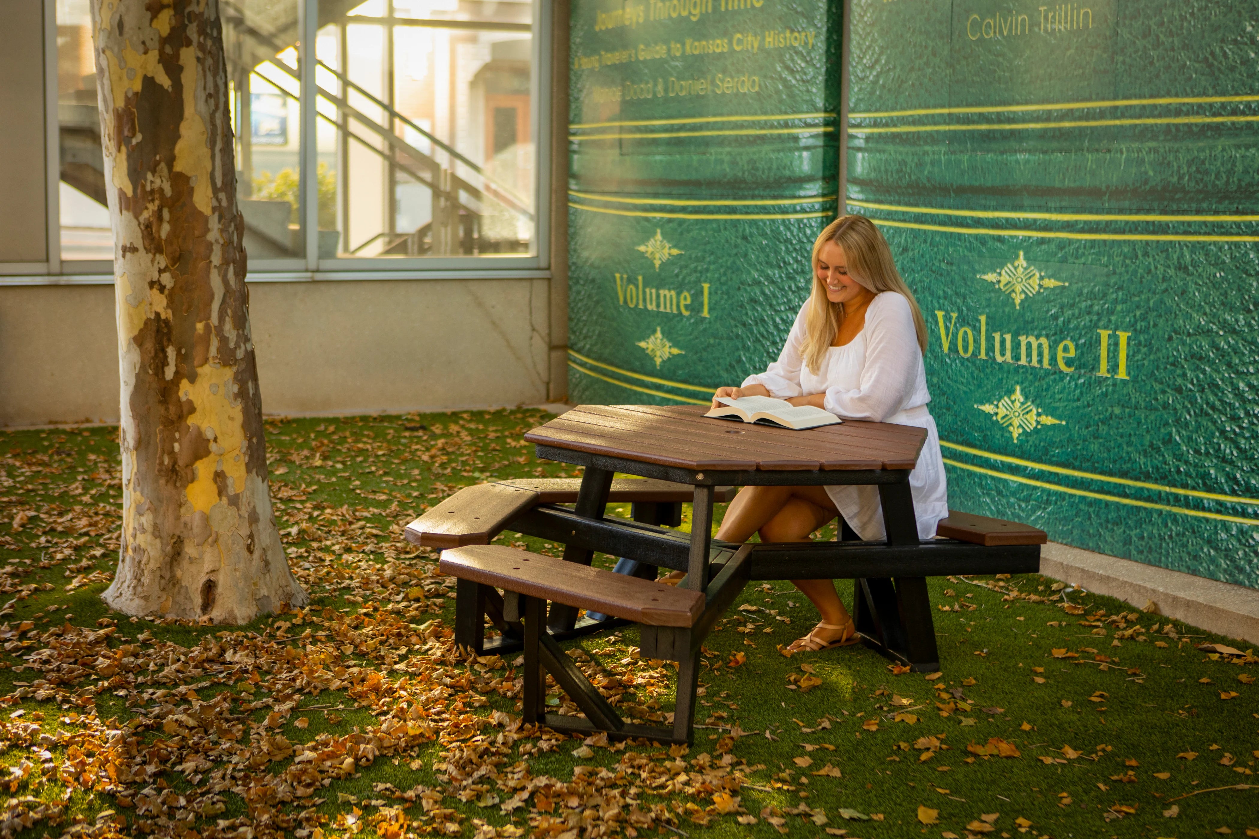 Woman sitting at a Frog Furnishings Hex Picnic Table reading a book in an outdoor setting.