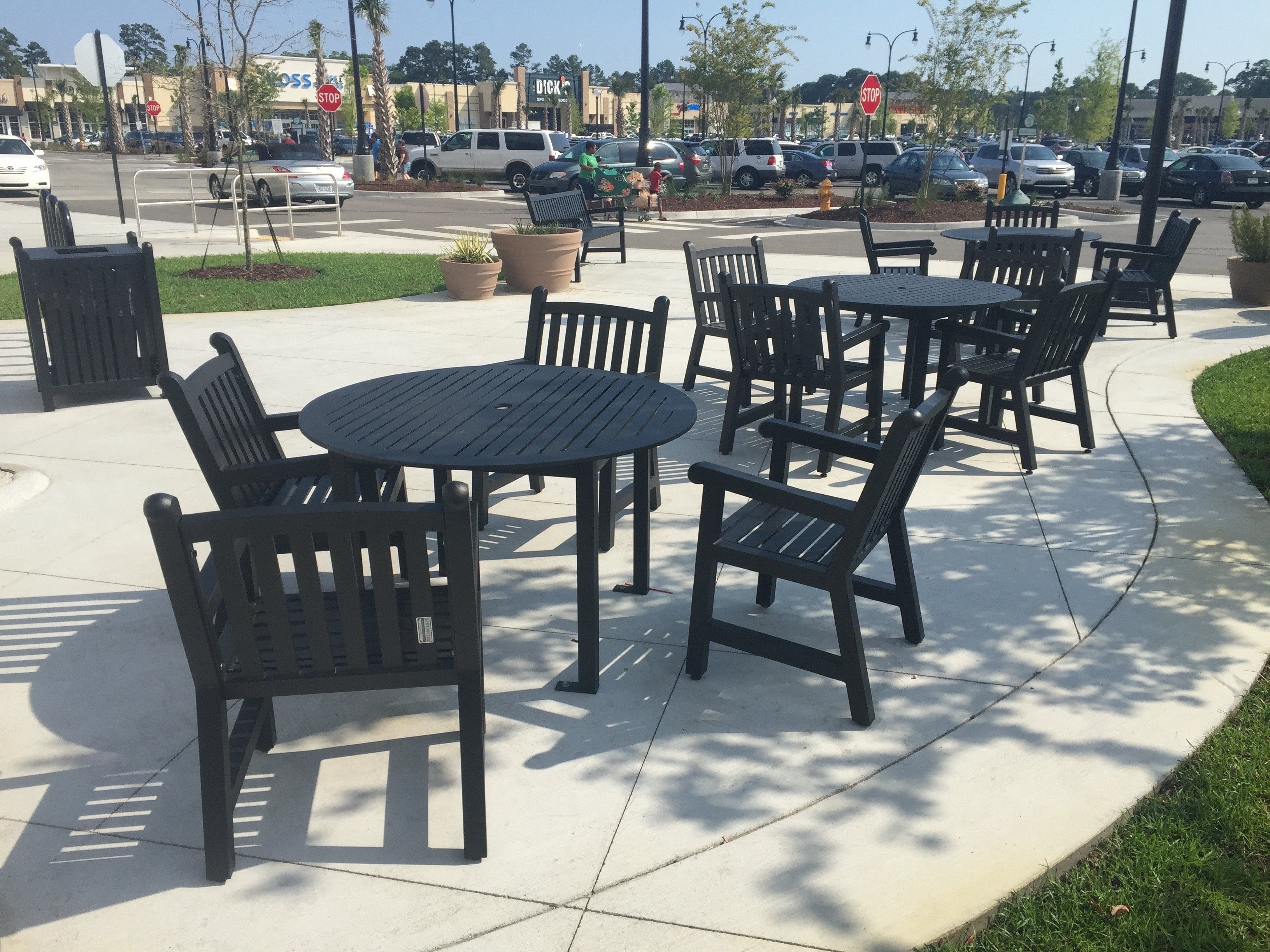 Black Yorktown dining chairs around 48 inch round slat tables on a shopping center plaza, model YO9113C, heavy duty patio furniture