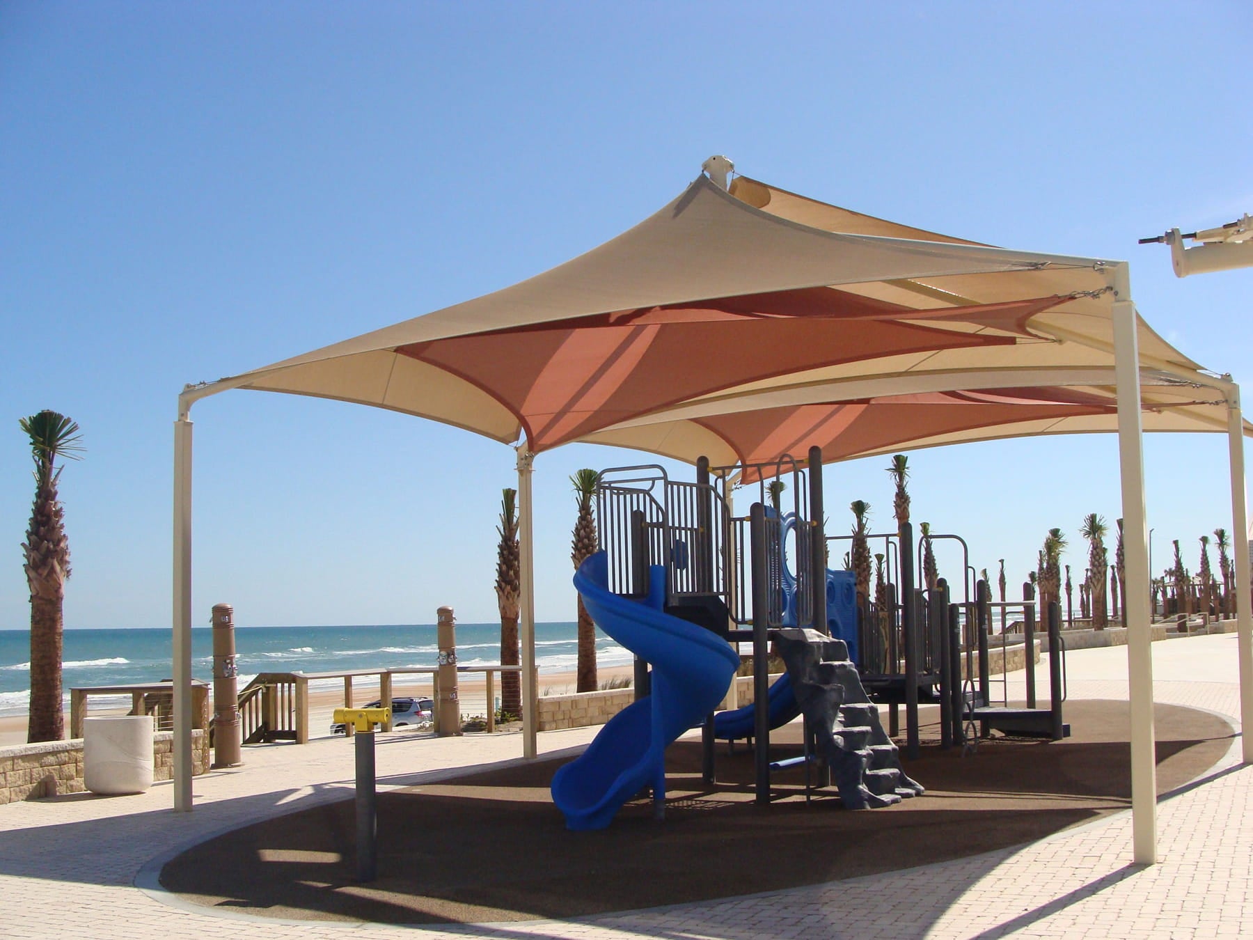 Children's playground with a large USA Shade Mariner Pyramid Shade overlooking the ocean.