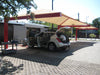 Car with open trunk at a gas station under a large red and beige USA Shade Full Hip Cantilever Shade.