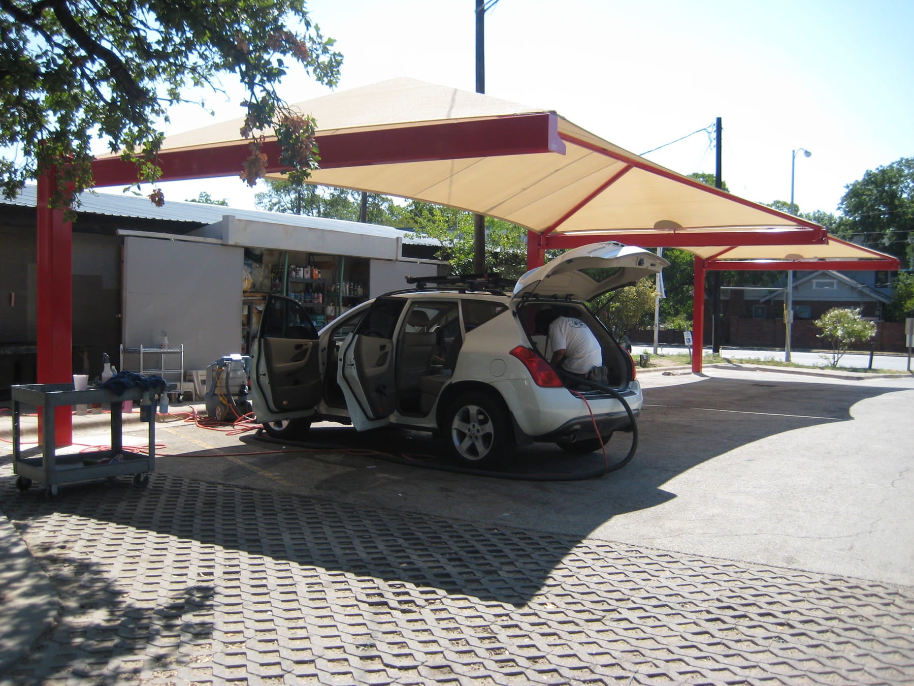 Car with open trunk at a gas station under a large red and beige USA Shade Full Hip Cantilever Shade.
