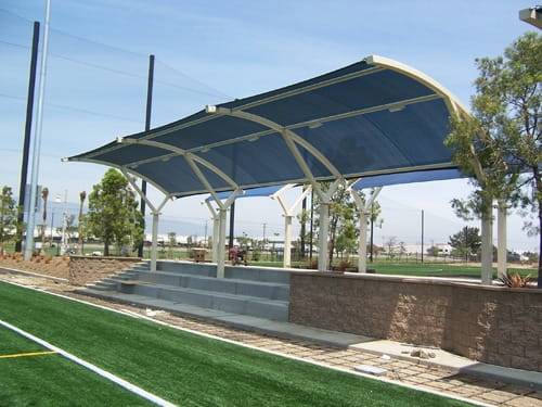 Outdoor sports facility with a USA Shade Eclipse Cantilever covered seating area and green grass