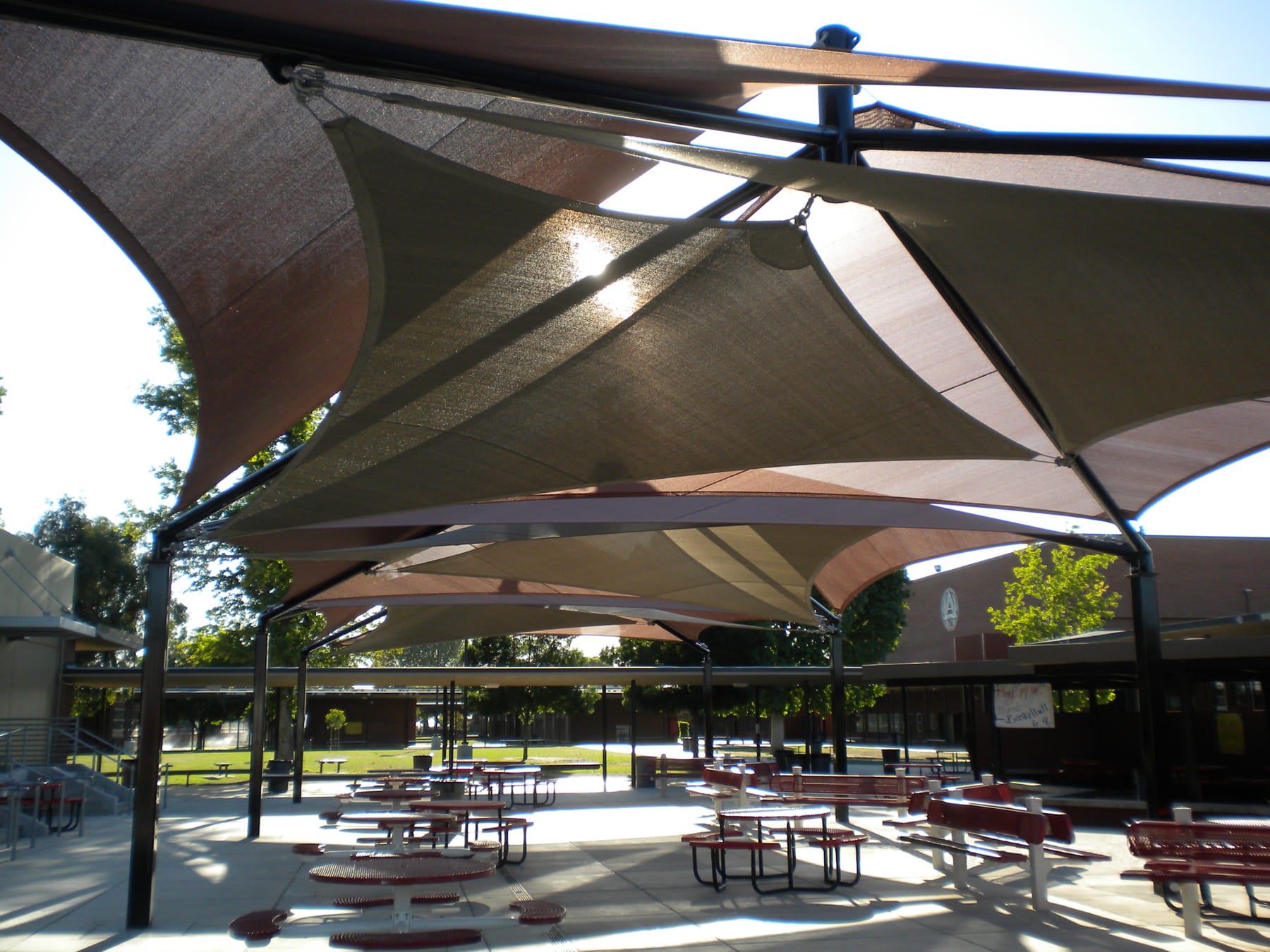 Outdoor shaded area with picnic tables and benches under large fabric USA Shade Mariner Pyramid Shade.