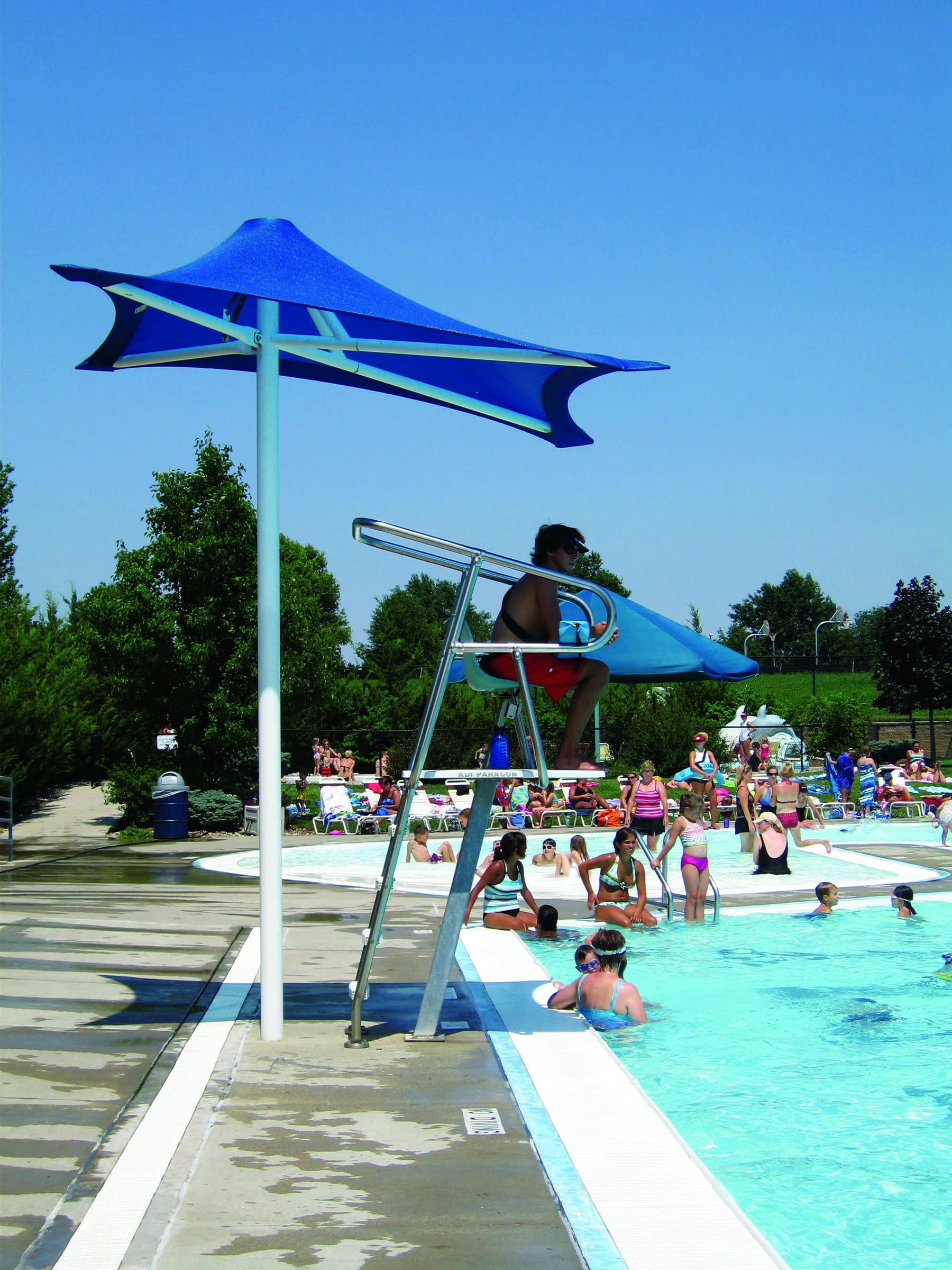People enjoying a pool day with a blue USA Shade Lifeguard Umbrella and lifeguard stand.