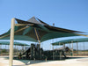 Outdoor playground with large USA Shade Multi-layer Super Span Pyramid Shade structures against a clear blue sky