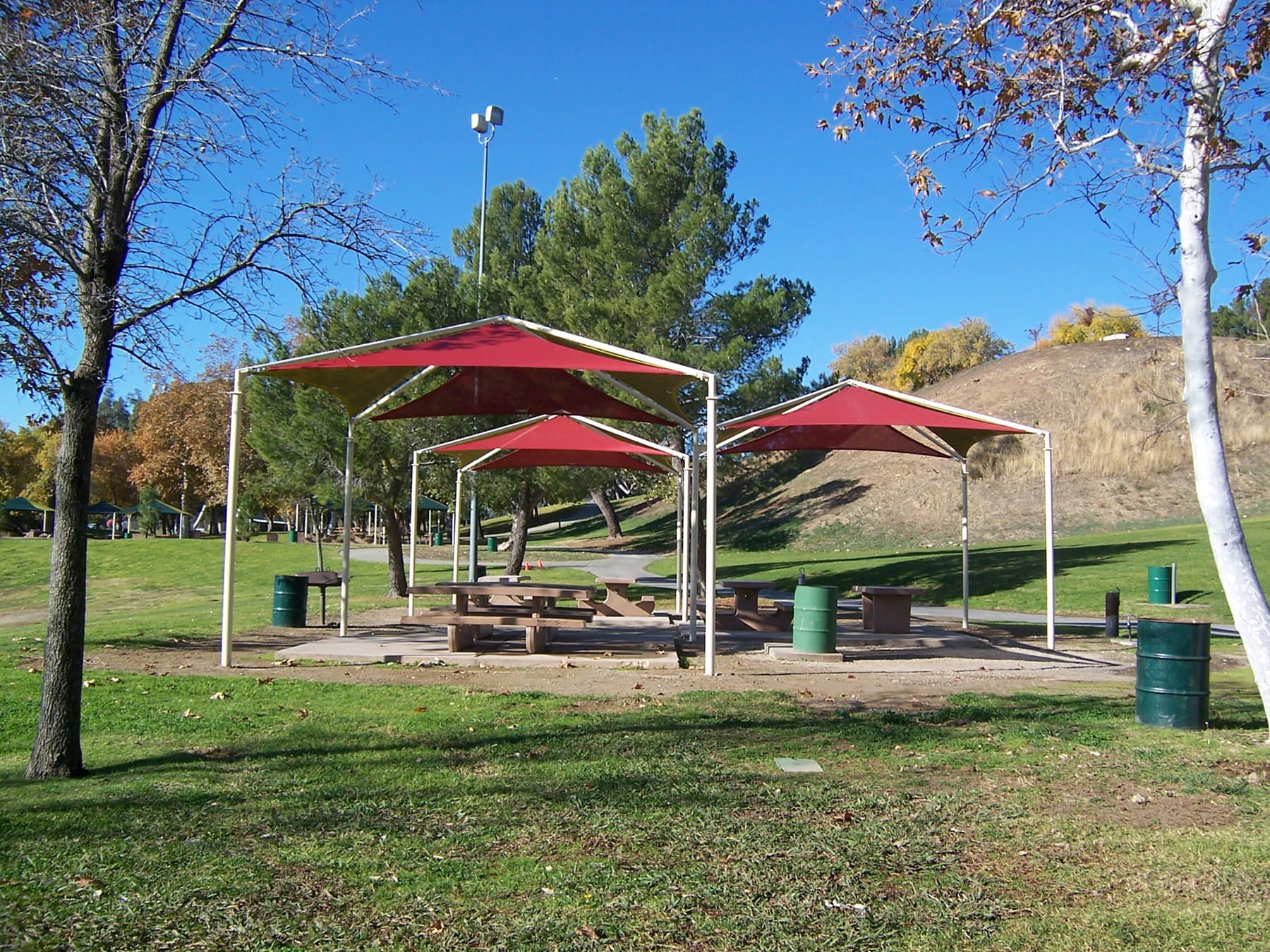Picnic area with red USA Shade Multi-Panel Pyramids and tables in a park setting
